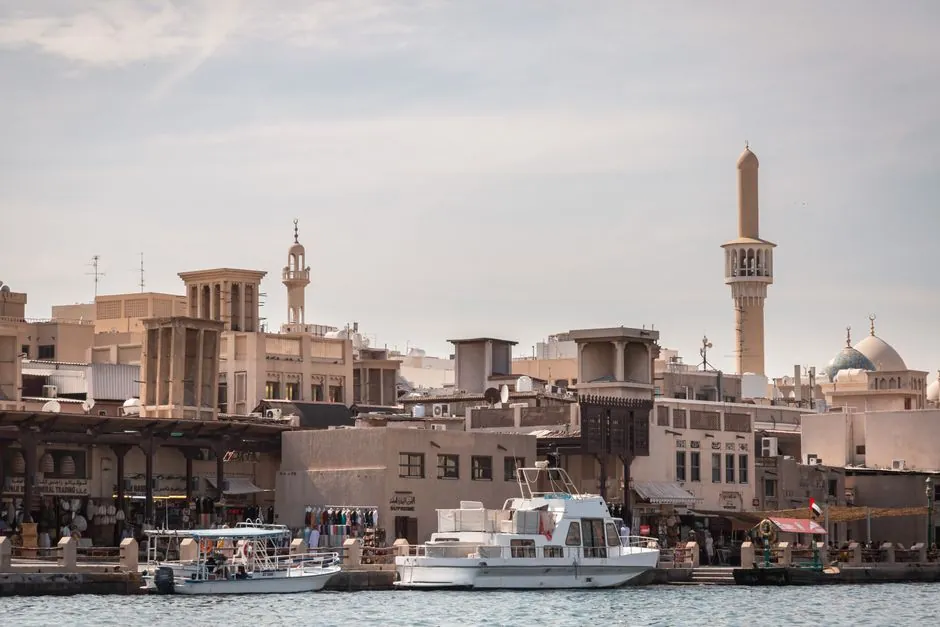 Bur Dubai's creekside seen from the water: wind-tower houses, souk shopfronts and the Grand Mosque minaret