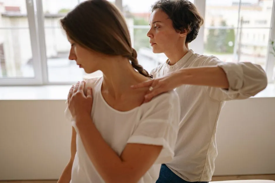 A female therapist checking a clothed, seated client's shoulder