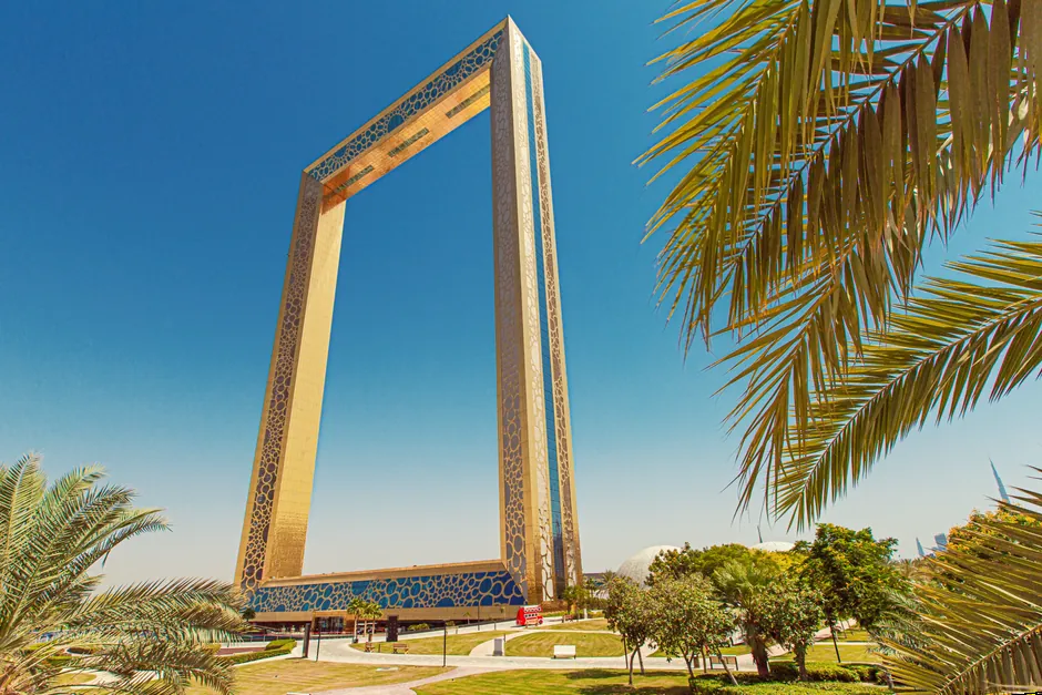 The Dubai Frame in Zabeel Park, framed by palm leaves against a clear blue sky
