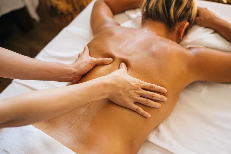 Hands pressing slowly beside a woman's shoulder blade as she lies face down on white linen