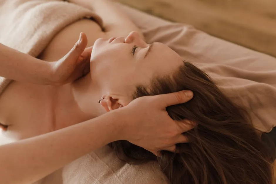 A female therapist's hands easing the neck of a woman lying on a bed