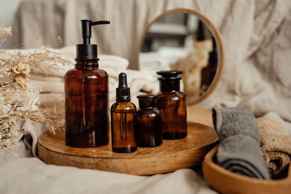 Amber oil bottles on a round wooden tray on linen, with rolled towels beside them